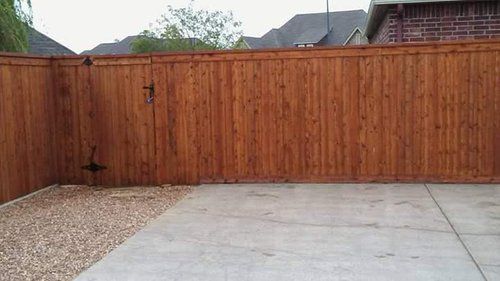 A wooden fence surrounds a concrete driveway in a backyard.