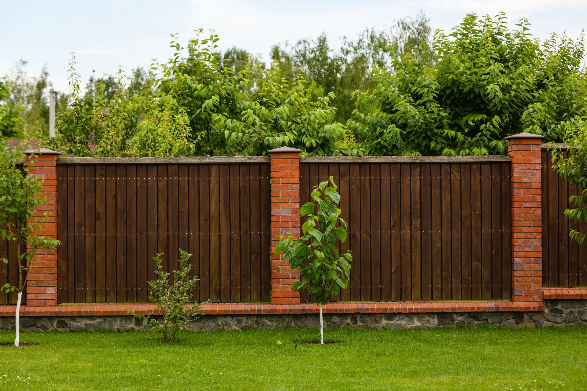 A wooden fence with brick posts in a lush green yard.