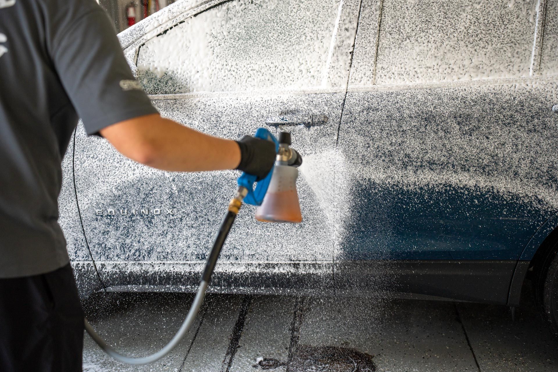 A man is spraying foam on a car with a spray bottle.