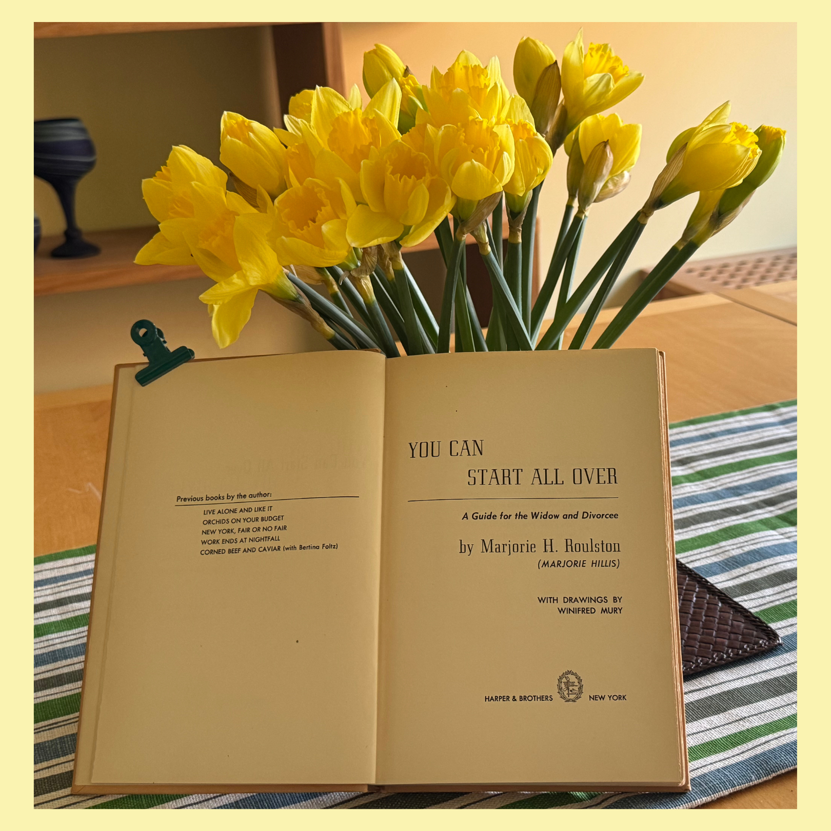 A bouquet of yellow daffodils sits behind an open book with the title 