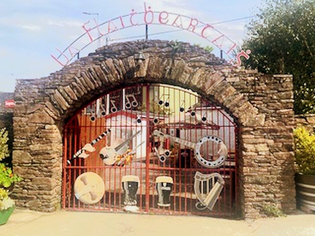 A stone archway entry with a metal gate decorated with musical instruments and two pints of beer under a curved sign.