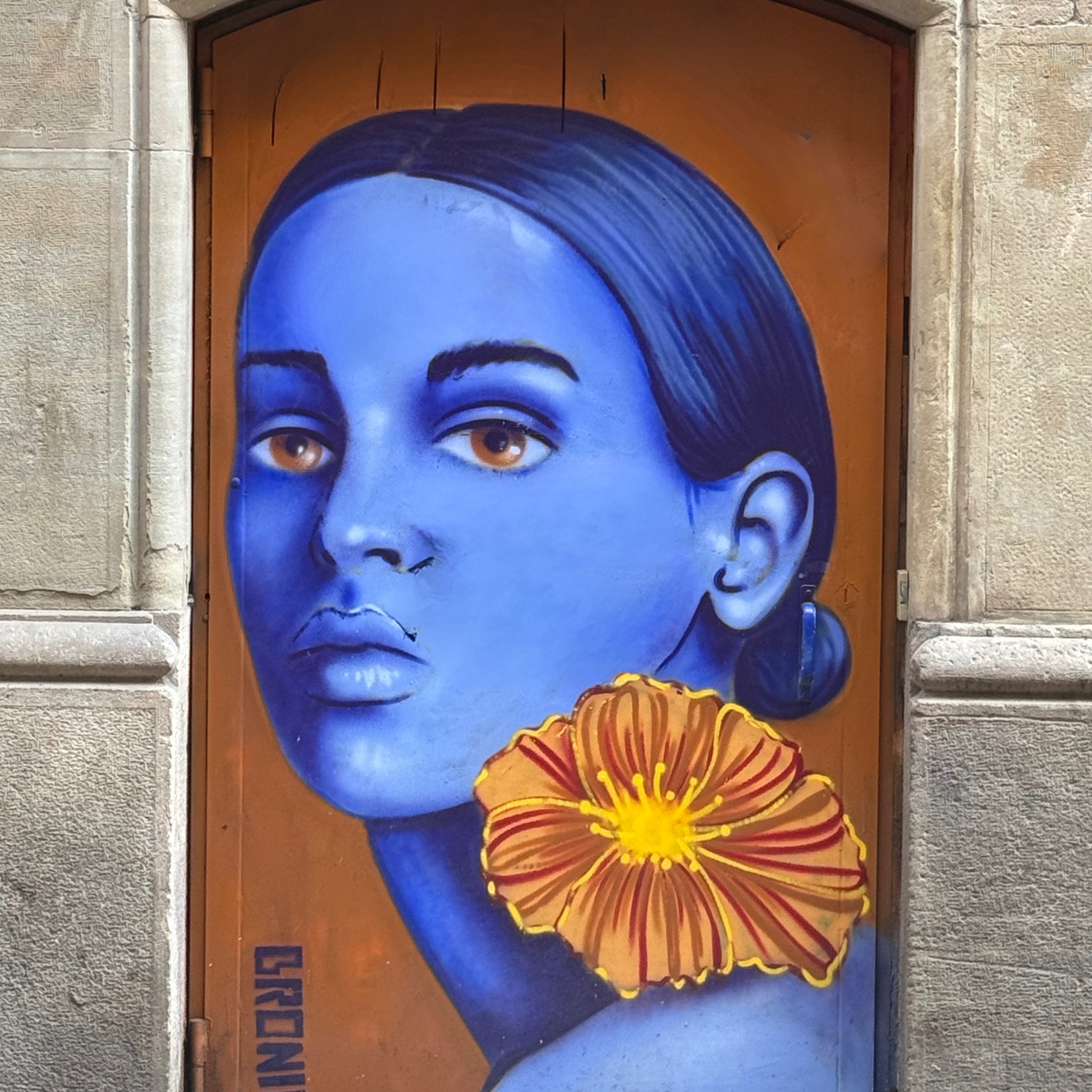 A mural of a person with blue skin and dark hair painted on an orange door, featuring a large orange flower at the neck.
