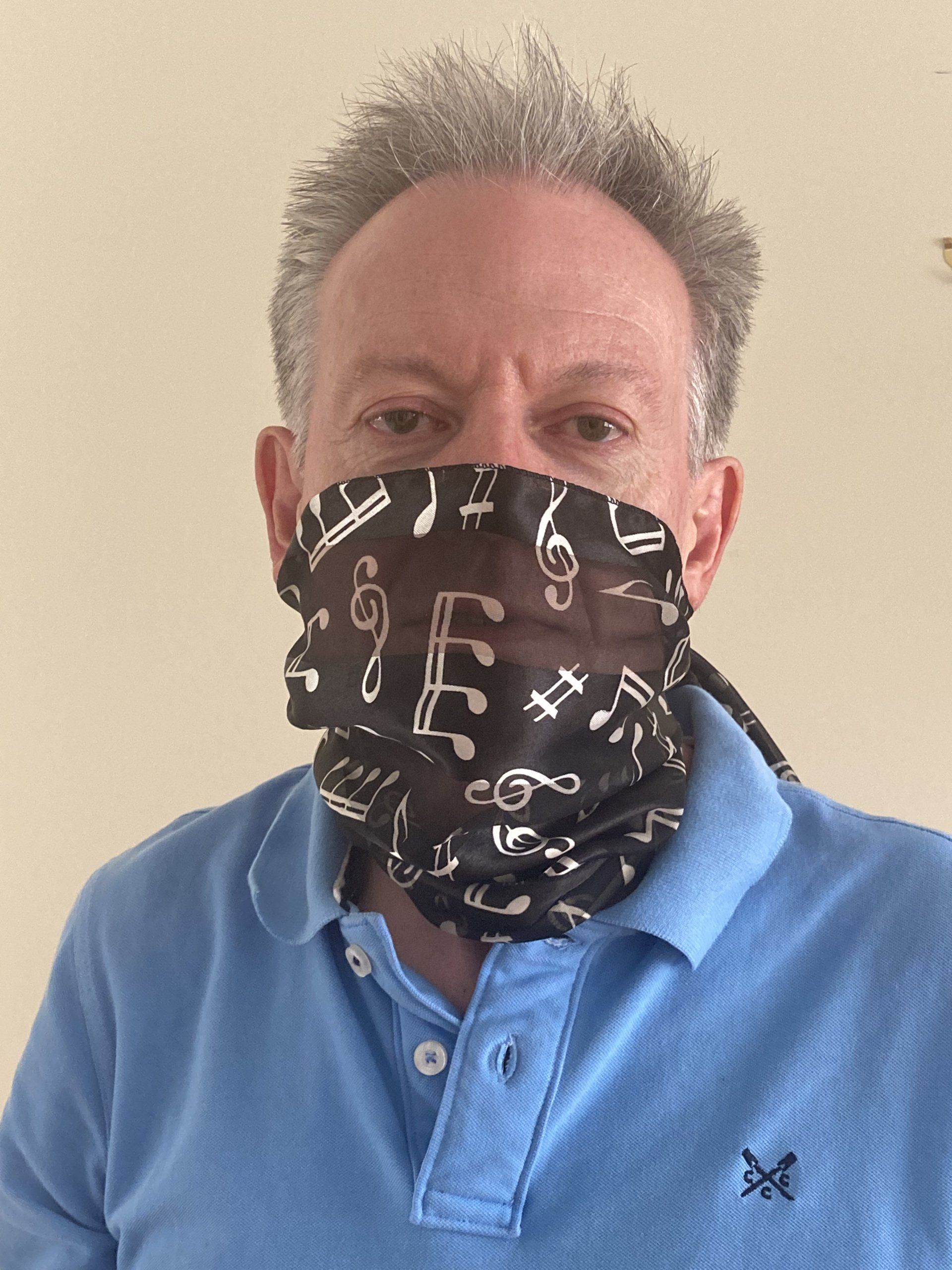 A person wearing a black neck gaiter decorated with white musical notes, paired with a light blue polo shirt.