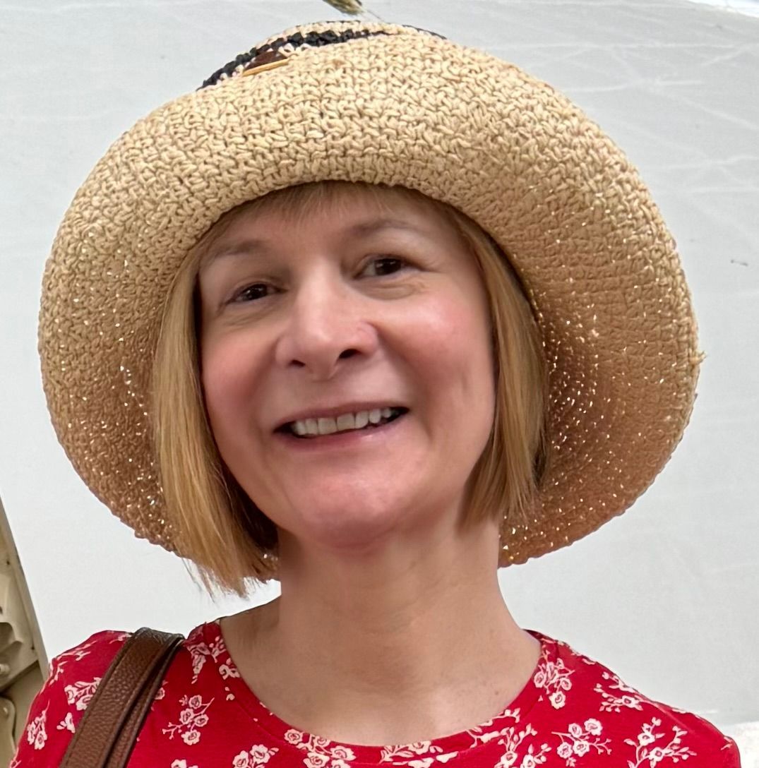 A smiling person wearing a straw hat and a red, floral-patterned shirt against a white background.