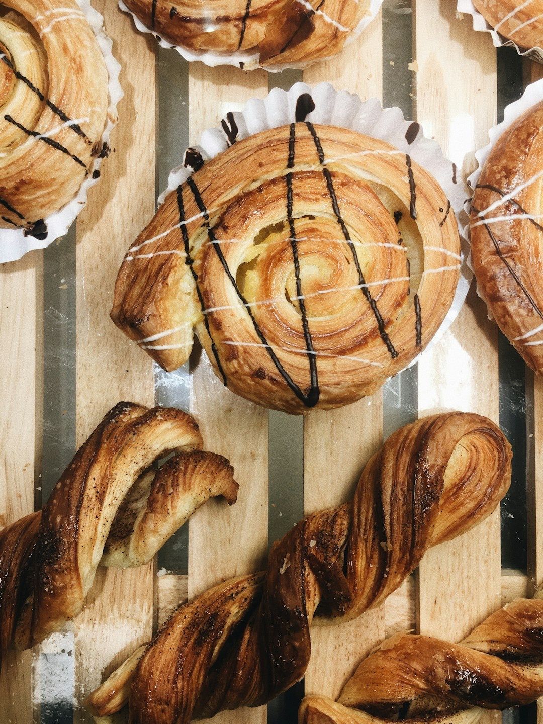 Top-down view of several pastries, including glazed snail-shaped buns and twisted danishes, on a wooden display rack.