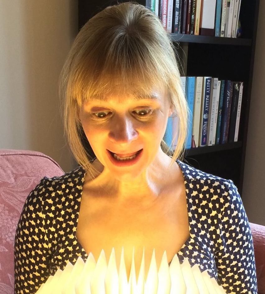 A person looks with a wide-eyed, surprised expression at a glowing, spiky paper object held in front of their face.