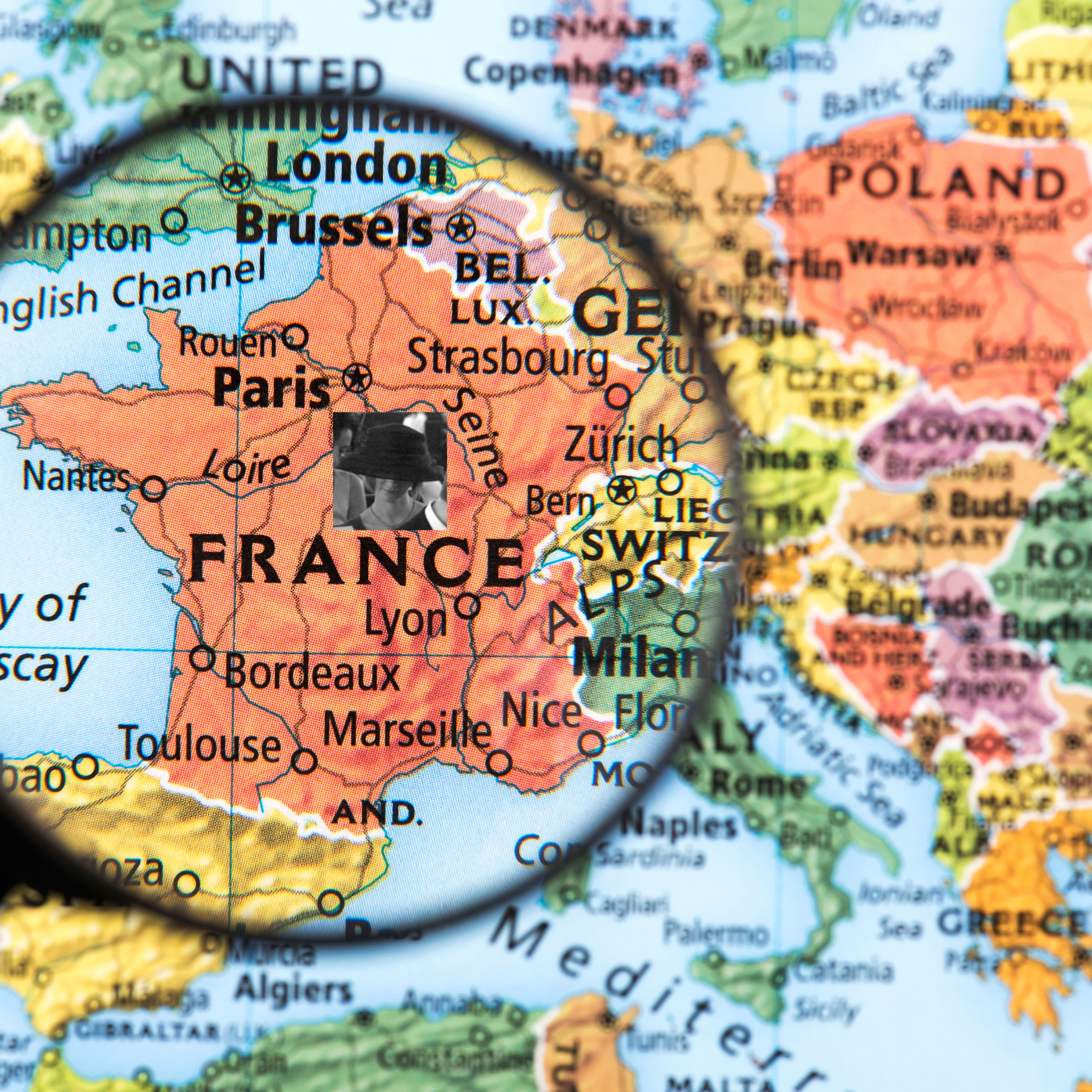 A magnifying glass focuses on France on a colorful map, with a small grayscale portrait embedded over the country.