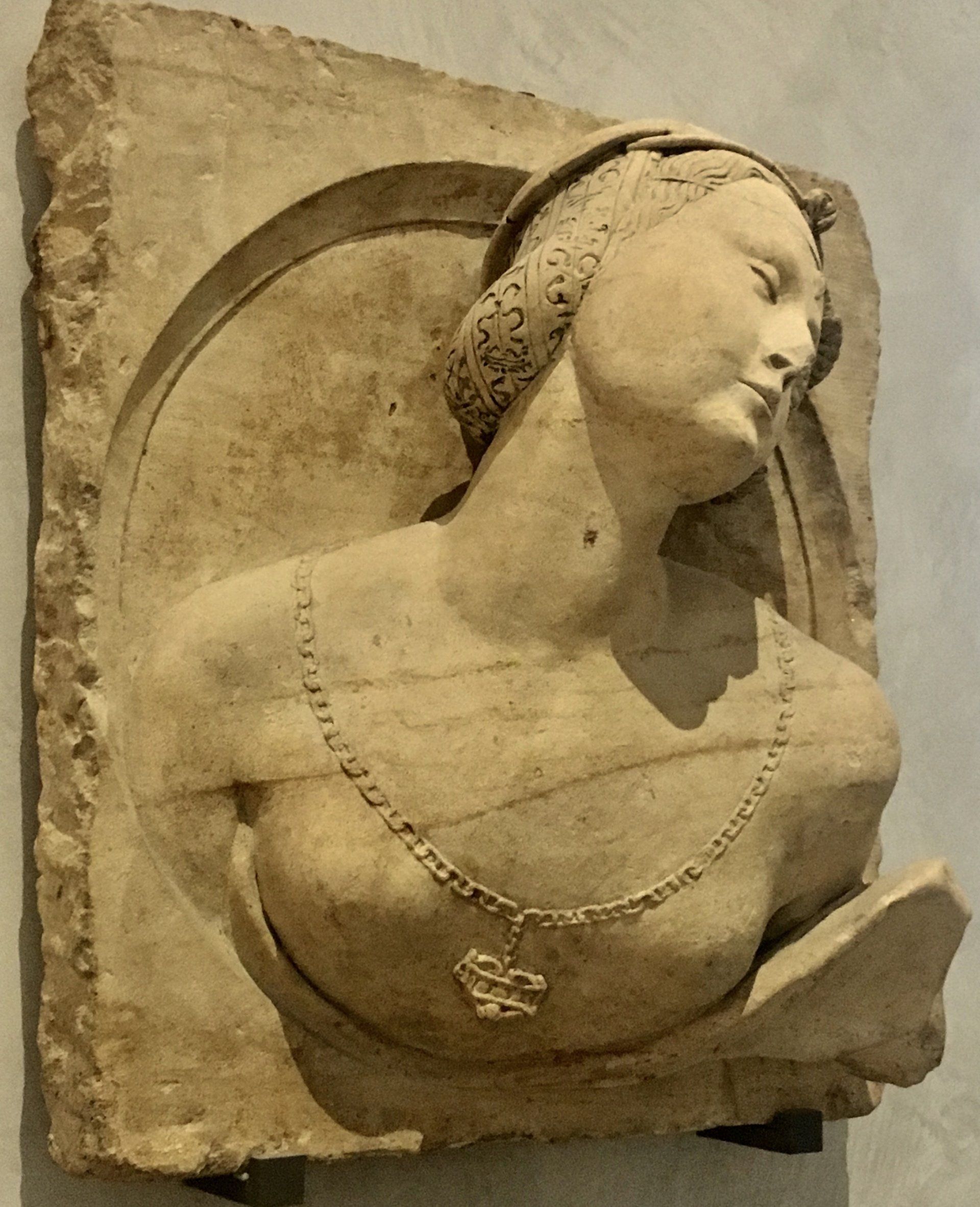 A stone relief sculpture depicting the upper torso of a person wearing a necklace, set within a rounded arch.