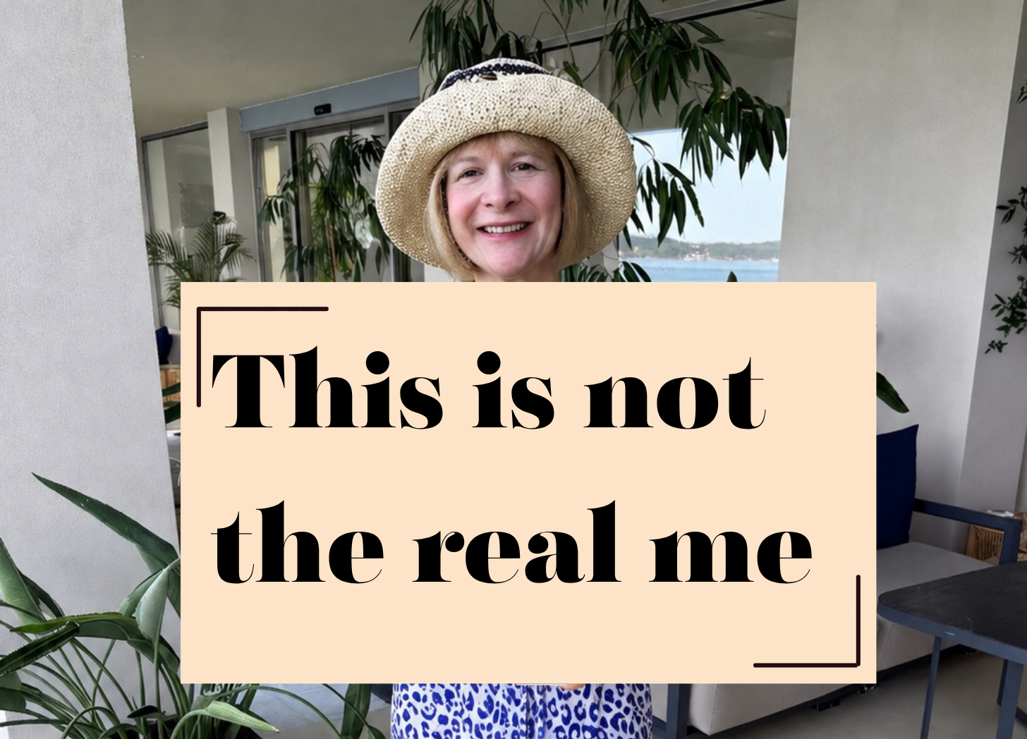 KatrinaRobinsonWriter in straw hat standing outdoors behind a sign reading “This is not the real me”