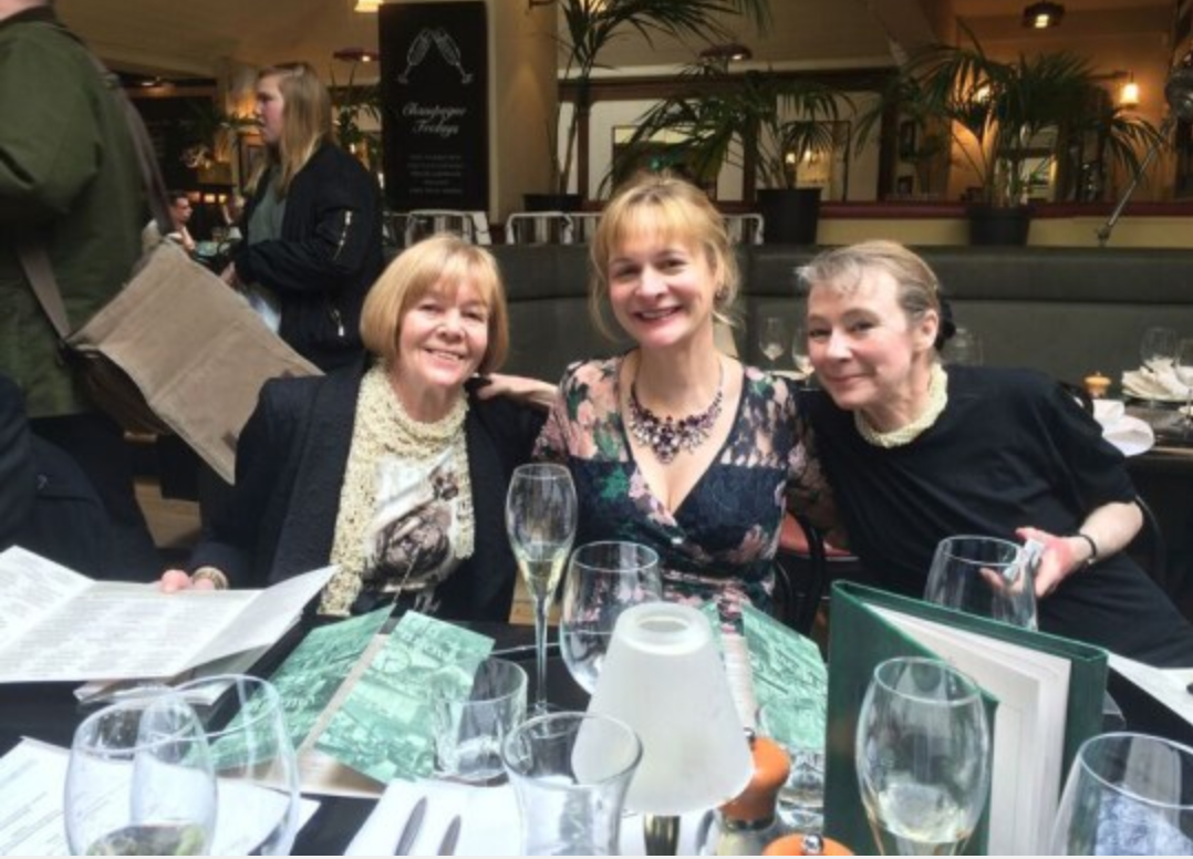 Three people smiling at a restaurant table, with drinks and menus in the foreground.