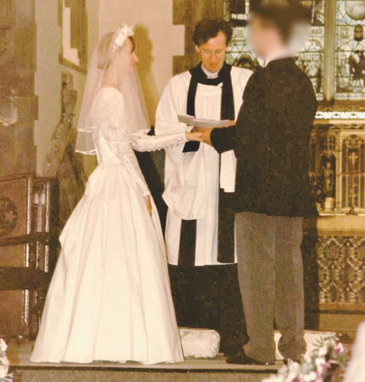 A bride and groom exchange wedding rings at the altar, presided over by an officiant in a church setting.