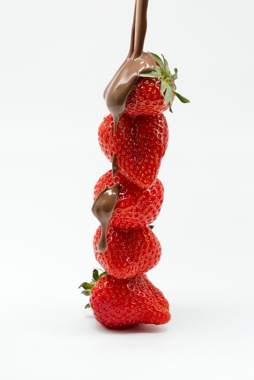 A vertical stack of five red strawberries against a white background with melted chocolate drizzling down the sides.
