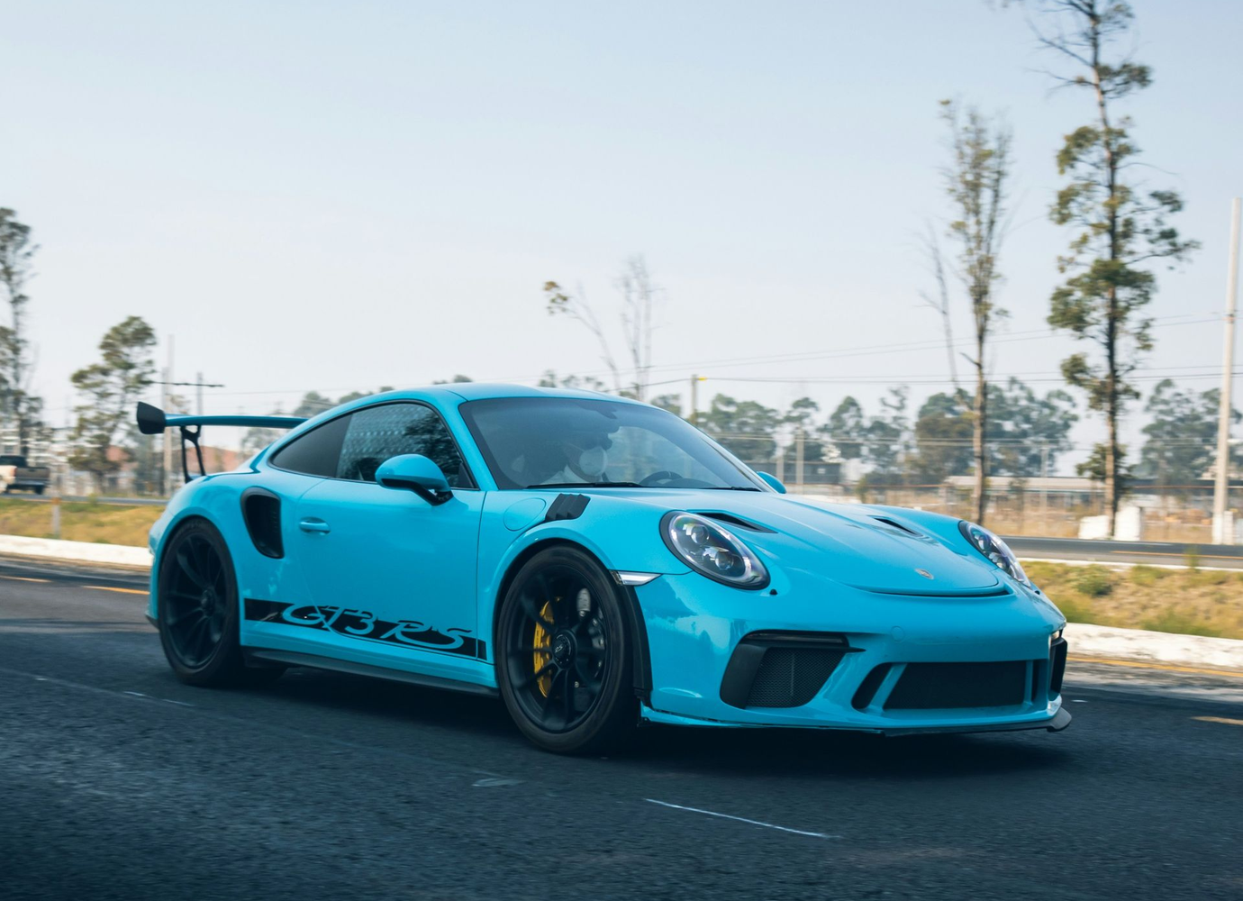 Blue Porsche GT3 RS sports car on a road, with black wheels and a rear spoiler.