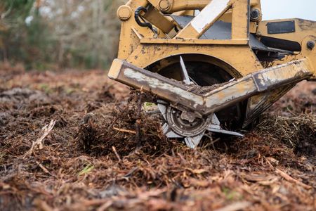 Yellow excavator blade pushing soil and debris on muddy ground
