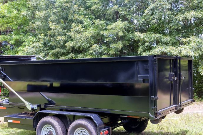 Black dump trailer parked on grass with trees in the background