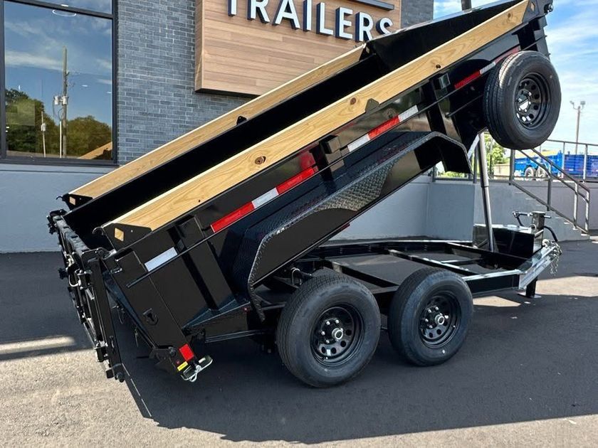 Black dump trailer with raised bed parked outside a trailer shop.