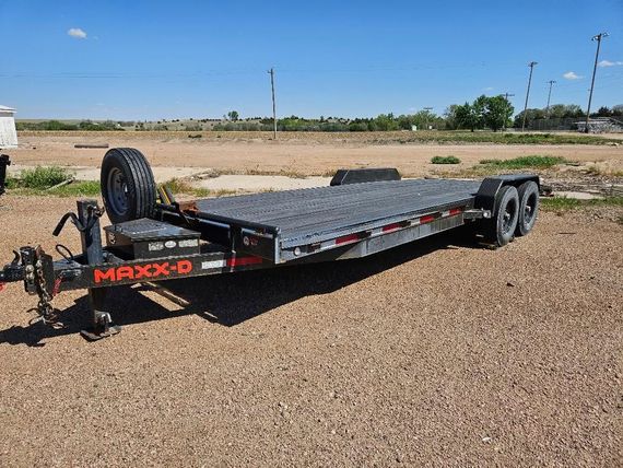 Black flatbed utility trailer parked on gravel in a field under a clear sky
