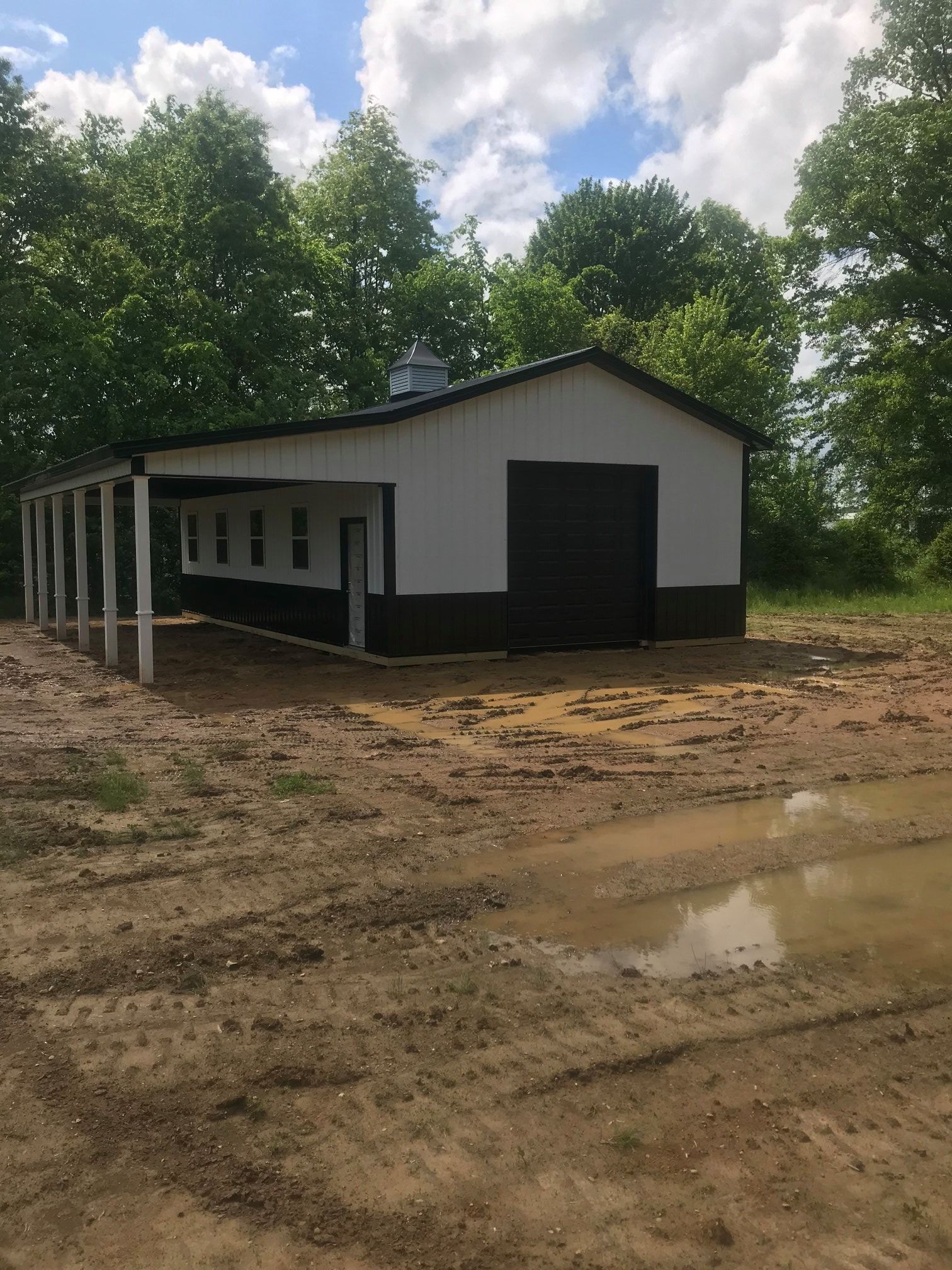 A white garage with a black door is sitting in the middle of a dirt field.