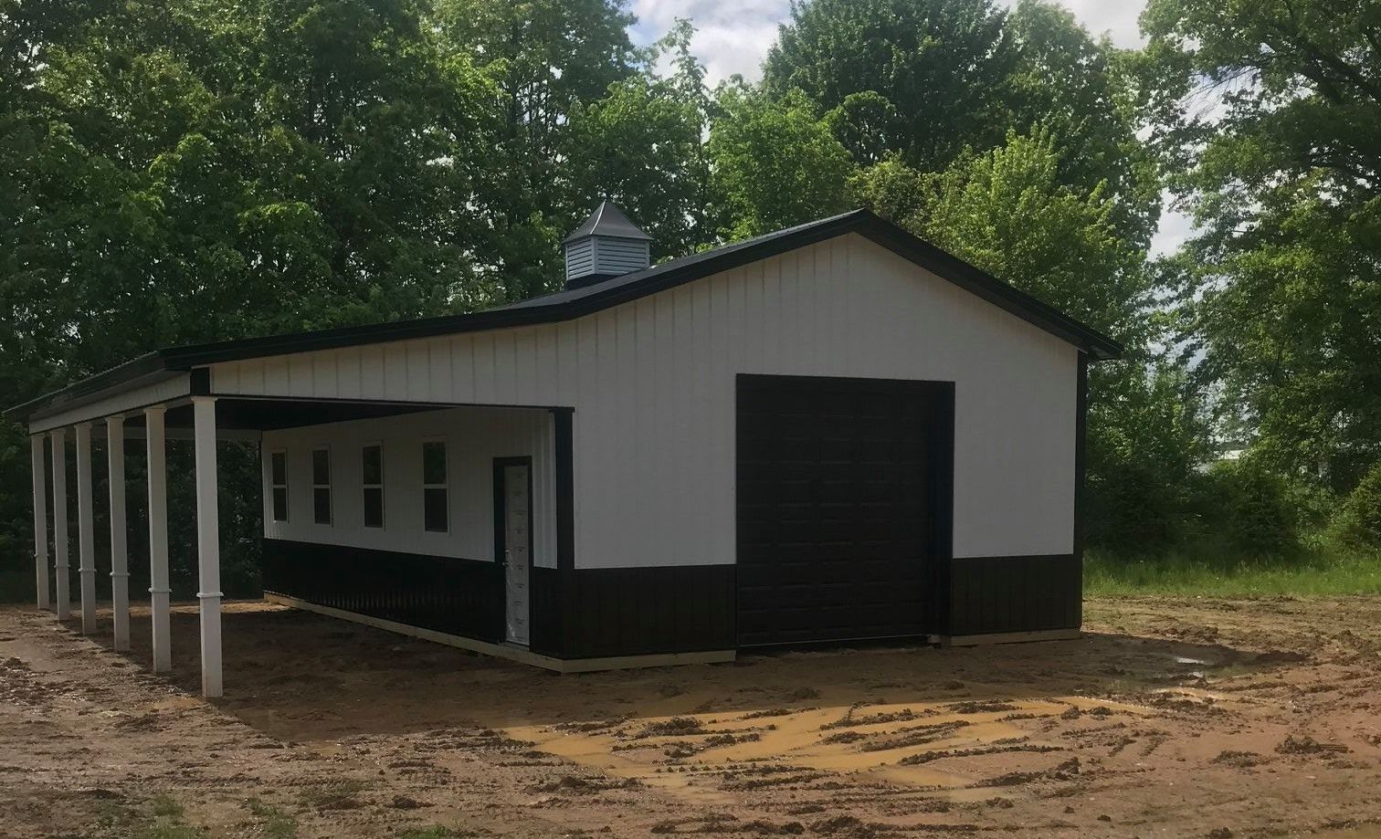A white and black building with a black garage door is sitting in the middle of a dirt field.