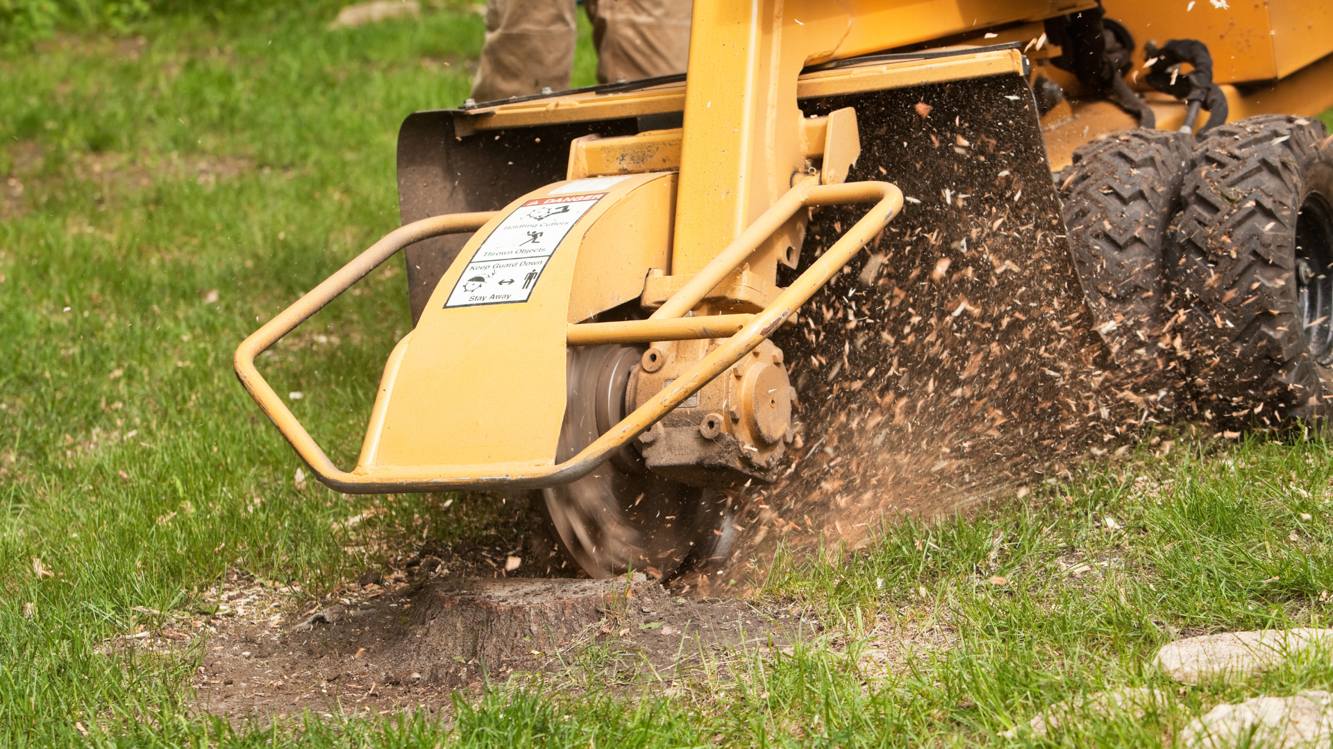 Yellow mower spraying grass and dirt while cutting a patch of lawn