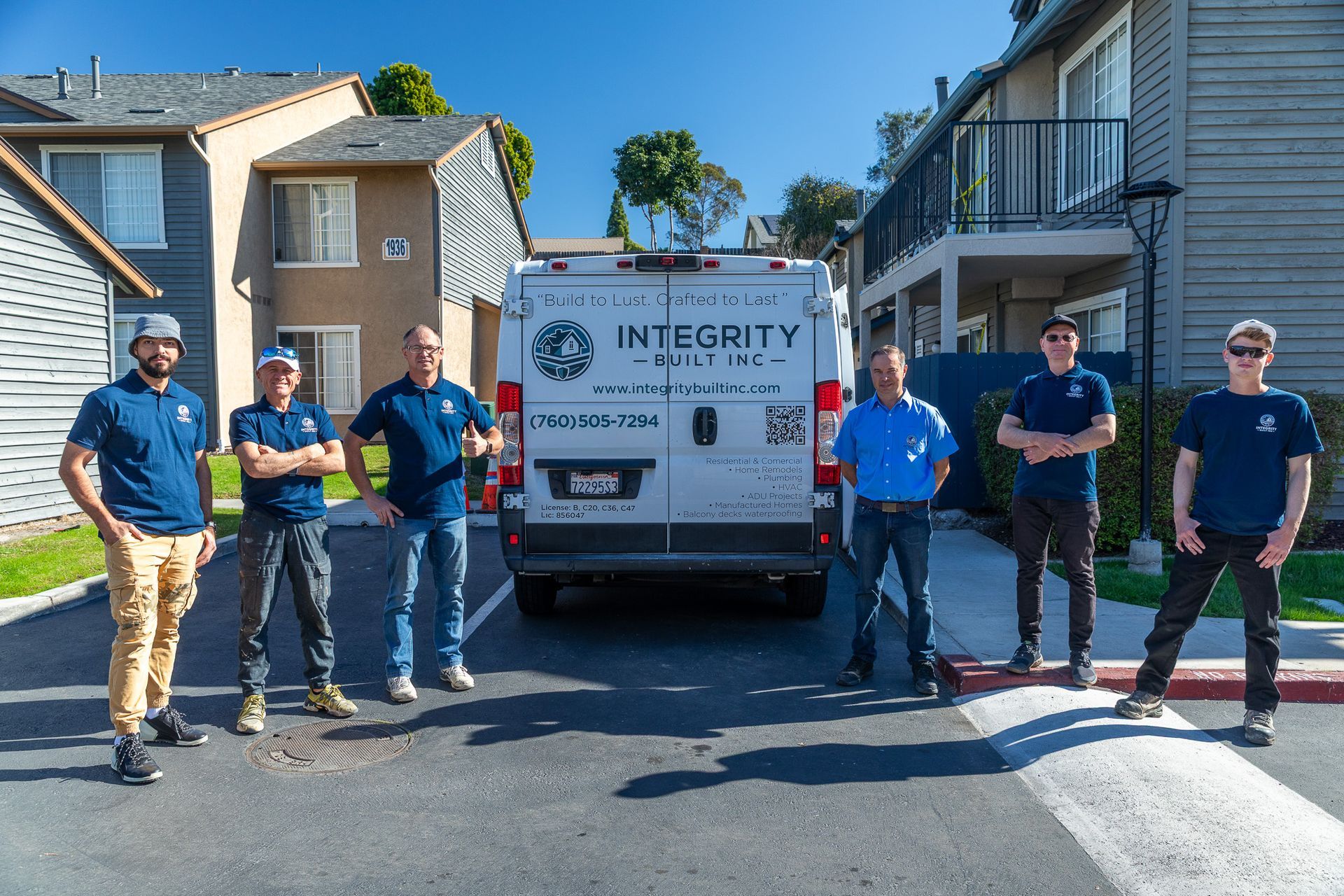 Group of men in blue shirts stand in front of a van. Buildings are in the background. Van has company logo.