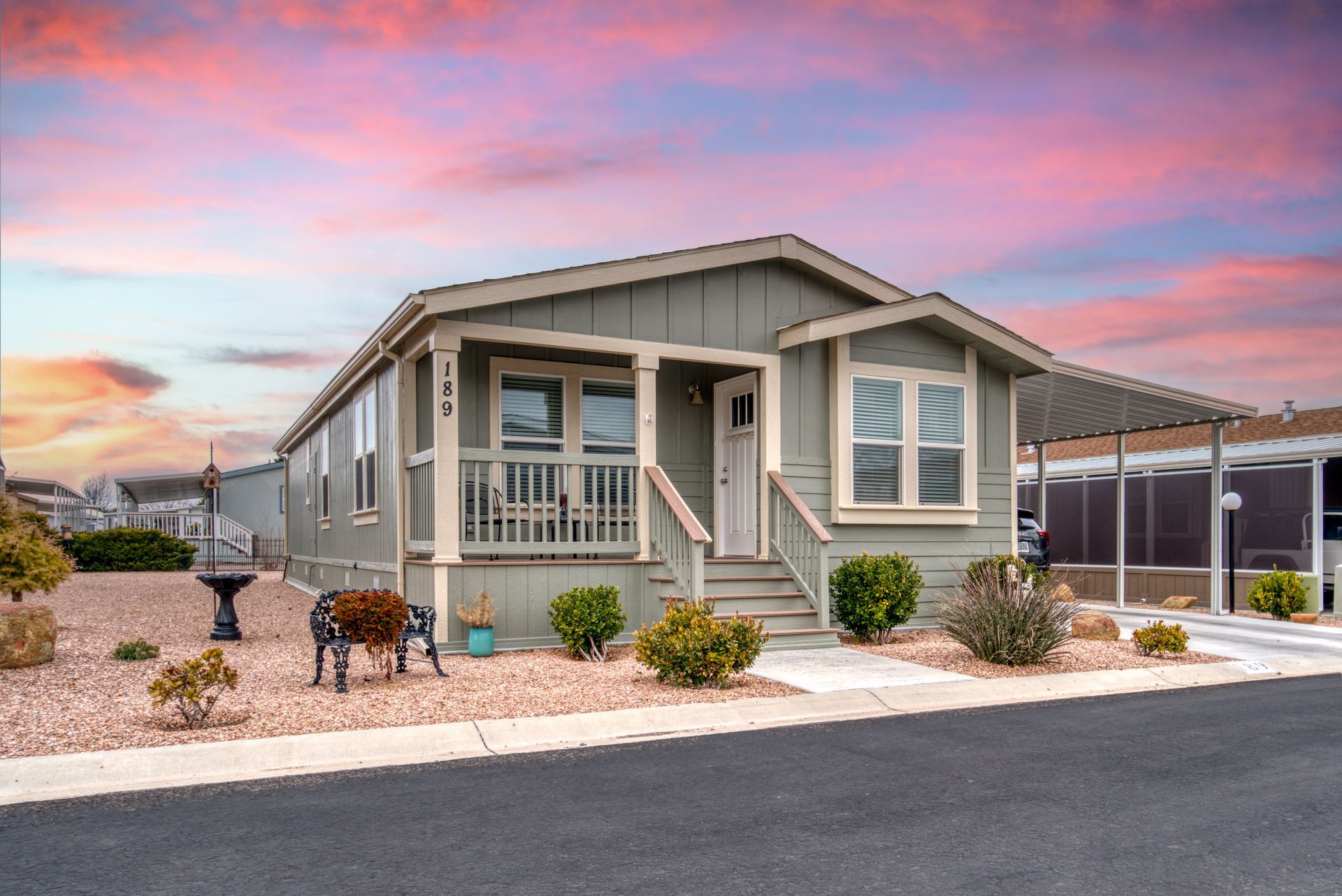 Green mobile home with porch, under a sunset sky.
