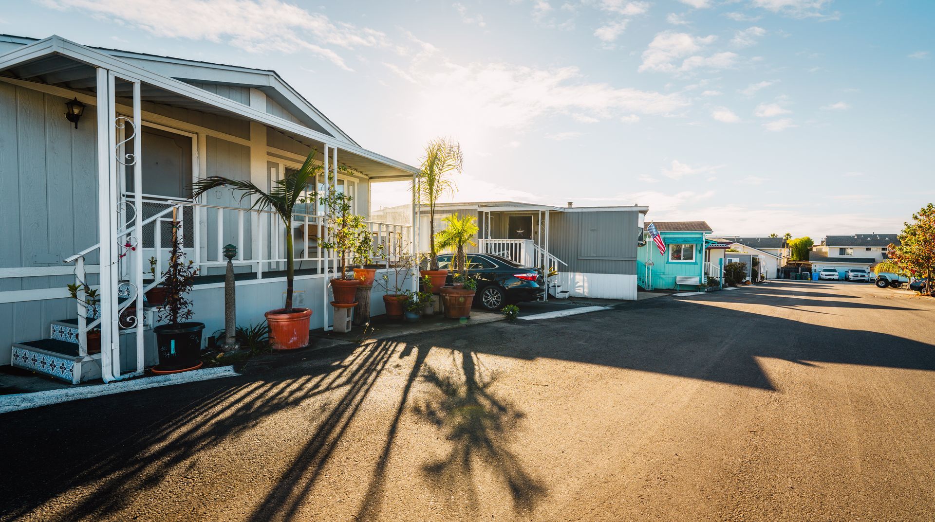 Mobile homes in a community; blue and white siding, parked cars, paved road, sunny day.