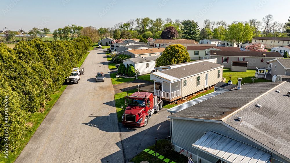 A mobile home being delivered on a semi-truck in a mobile home park on a sunny day.