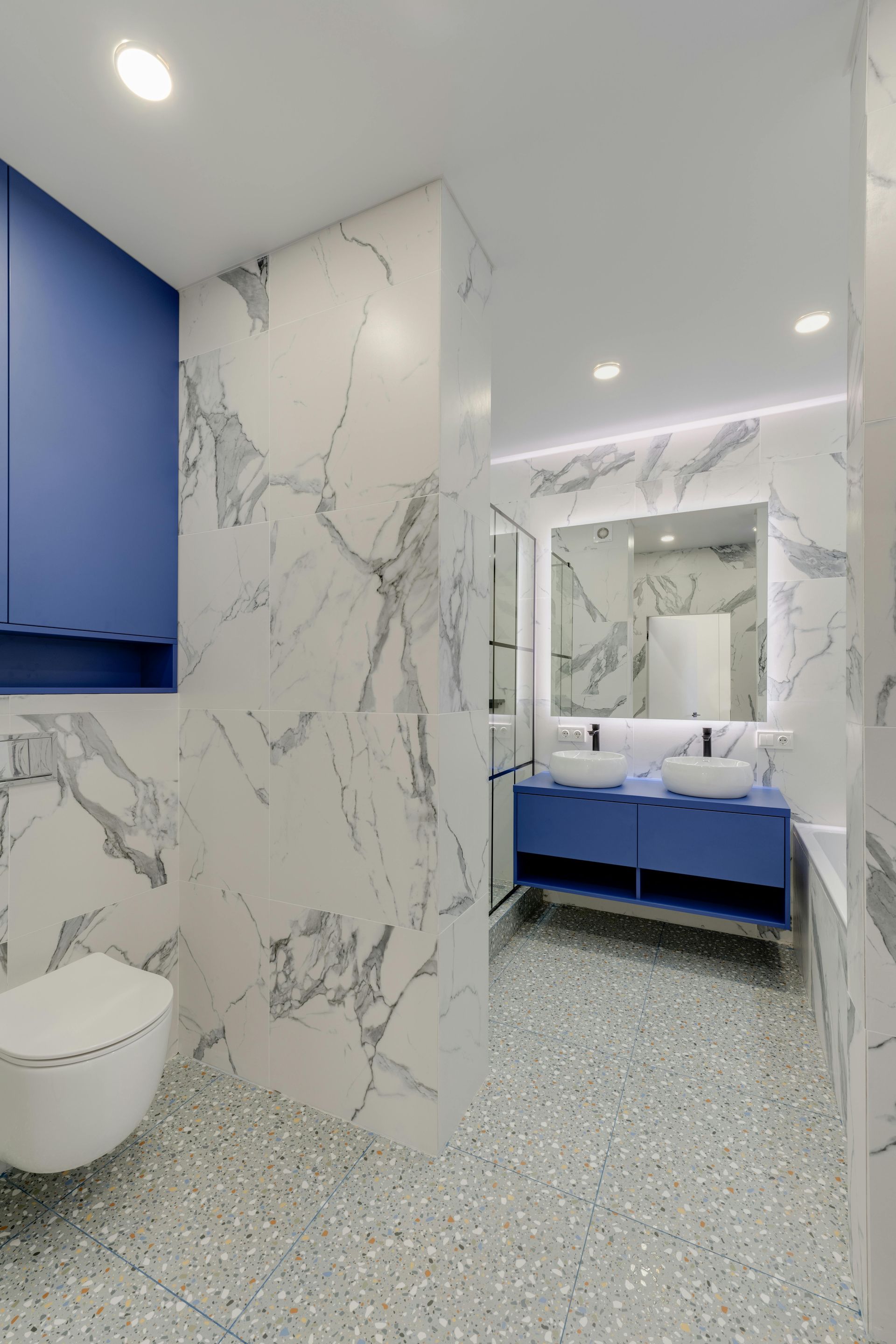 Modern bathroom with blue cabinetry, marble walls, and terrazzo flooring.