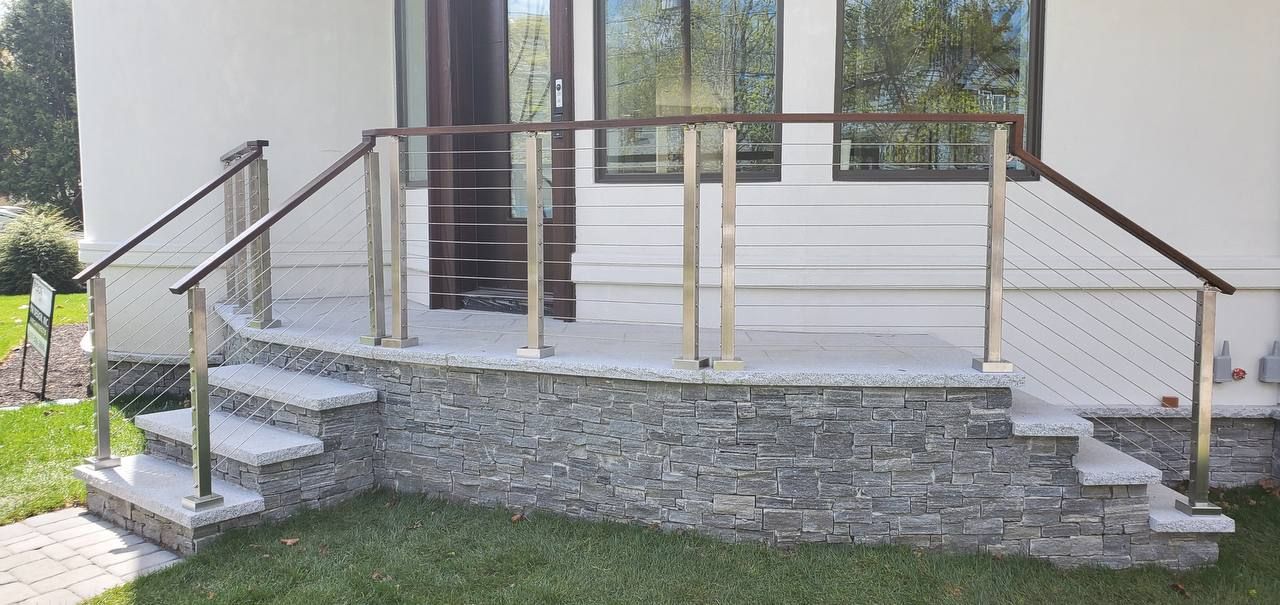 A house entrance with stone steps, gray stone facade, and metal railings with a wooden top rail.