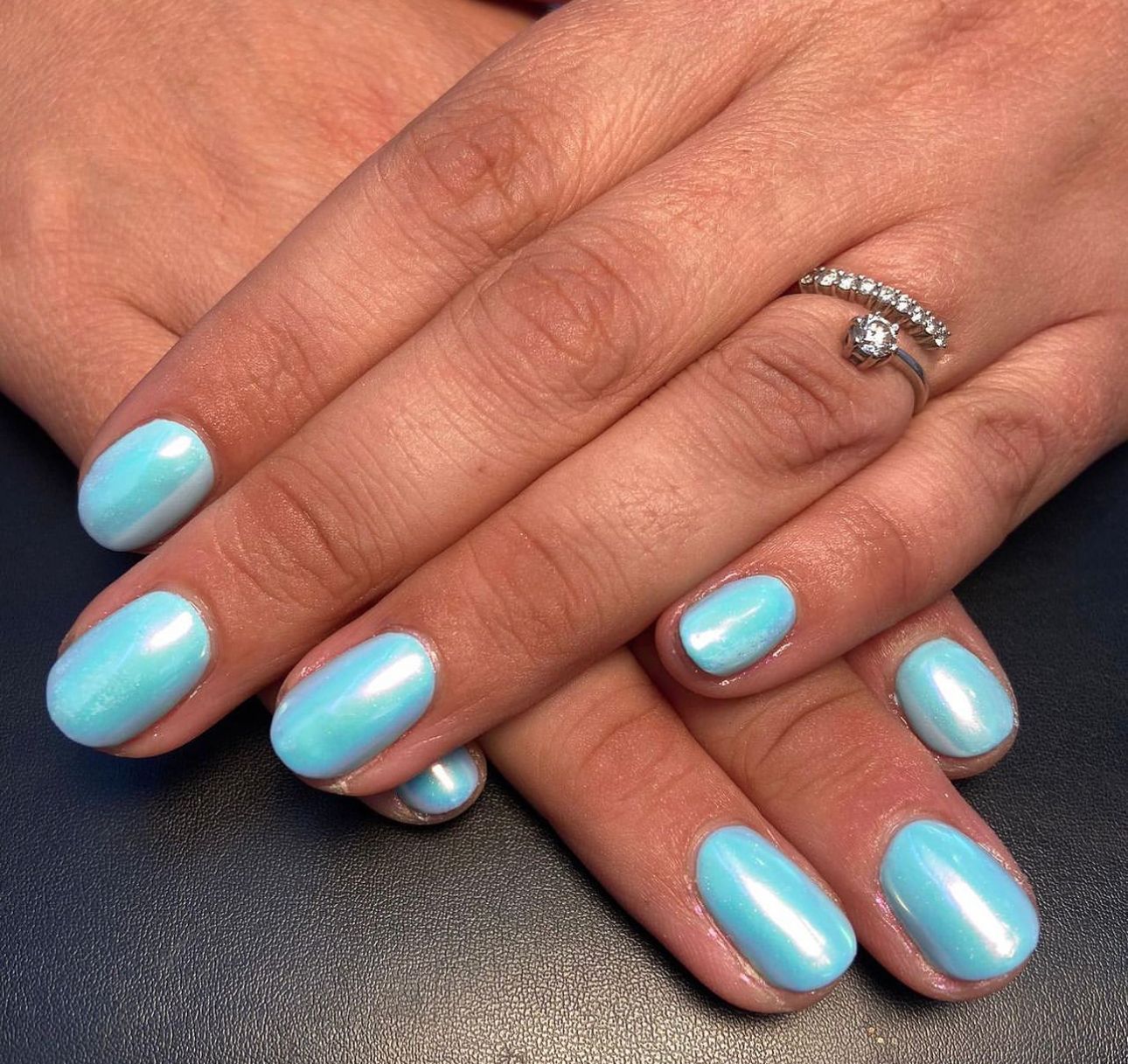 Hands with short, rounded nails painted in a glossy, light turquoise blue color.