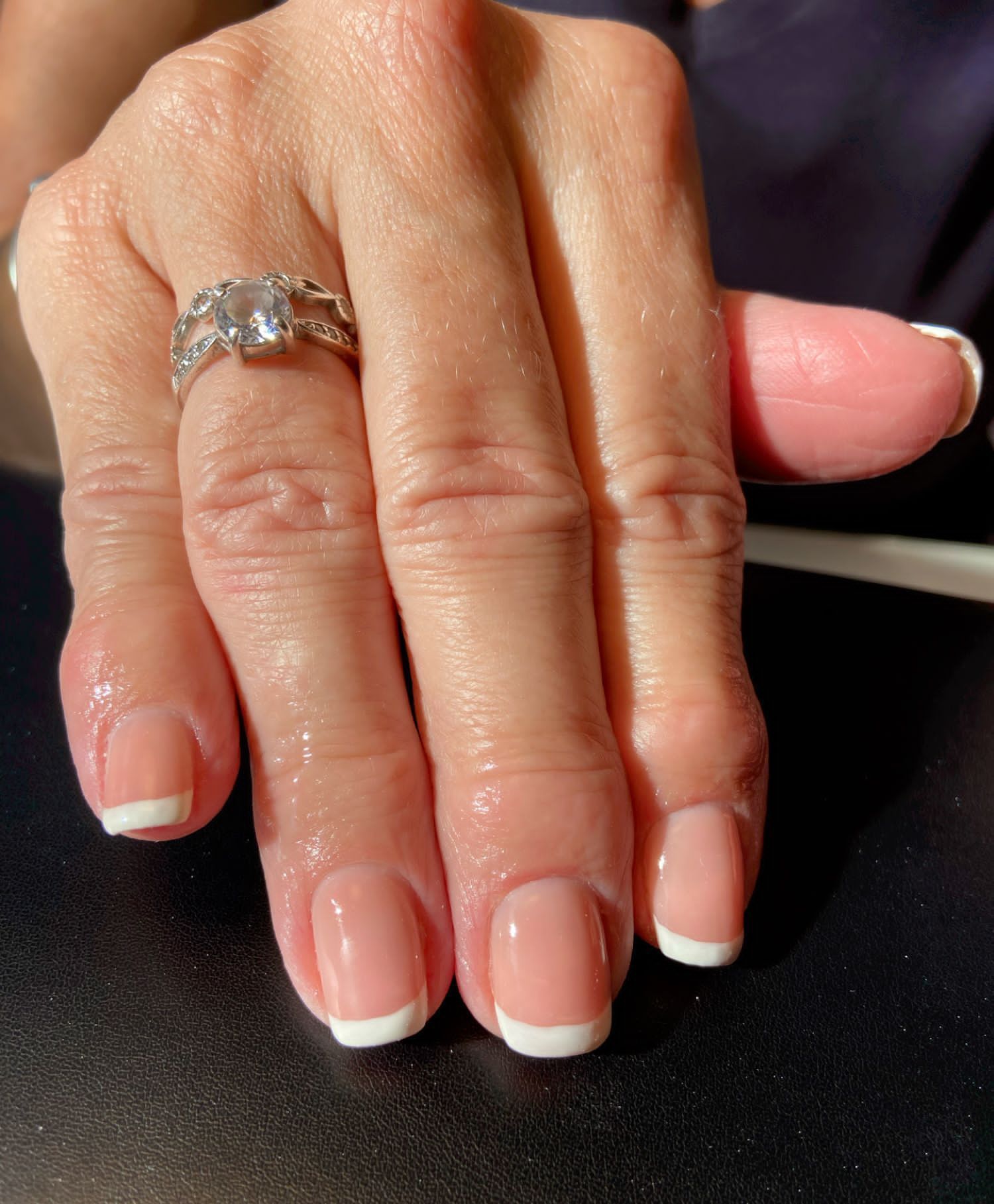 A hand with a French manicure, featuring a silver ring on the ring finger, resting against a dark surface.