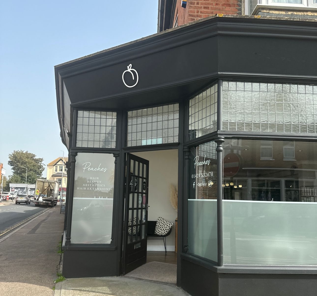 A black corner storefront featuring a white peach logo above the entrance and glass windows on a sunny street.