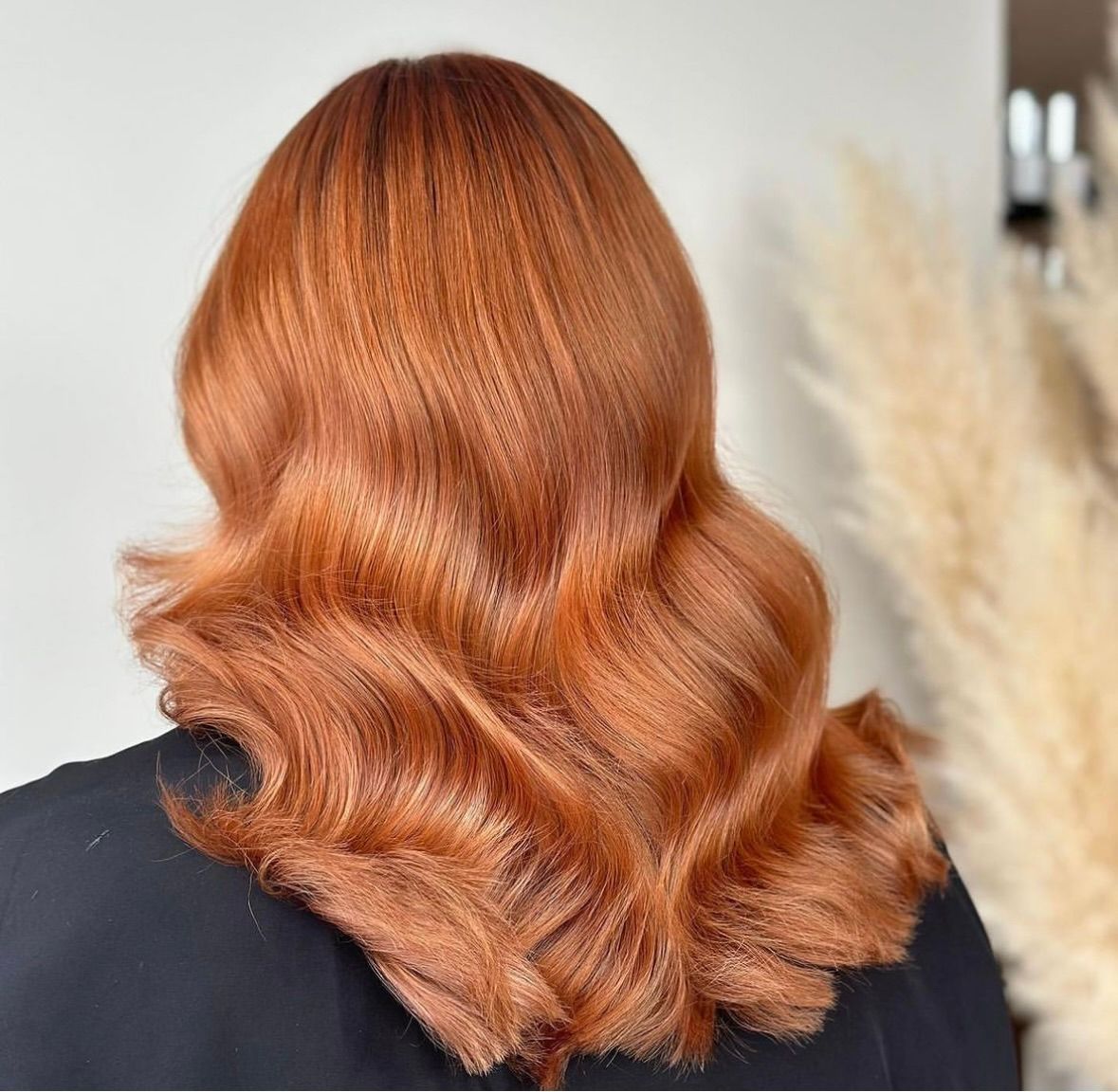 A back view of hair styled in soft waves with a vibrant, copper-red color and textured, crimped sections.
