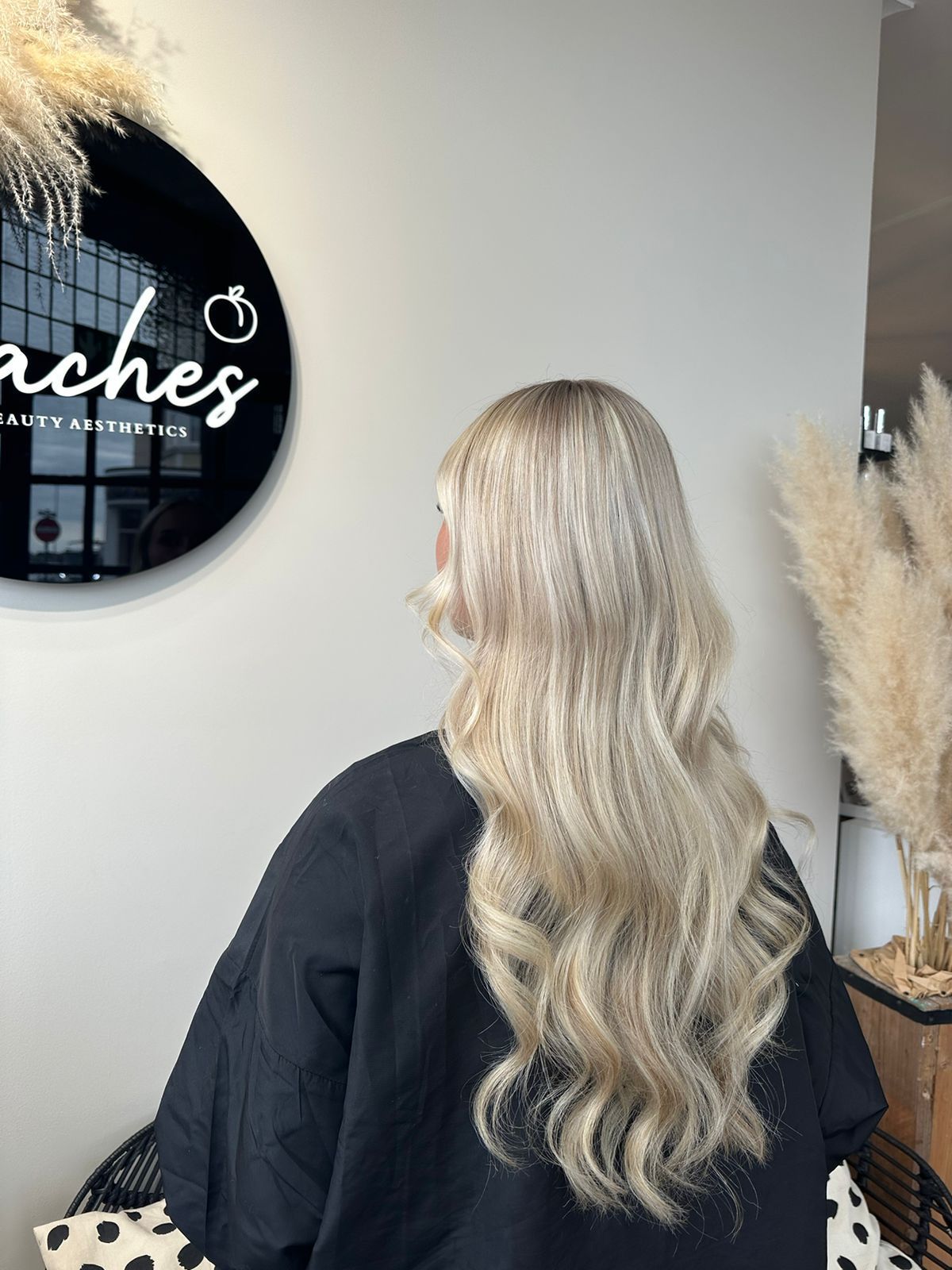 A person from behind displaying long, wavy, ash-blonde hair in a hair salon.