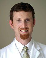 A man with a beard is wearing a white coat and tie.