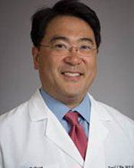 A man in a white coat and tie is smiling for the camera.