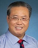 A man wearing glasses and a tie is smiling for the camera.