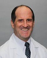 A man in a white coat and tie is smiling for the camera.