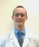 A man in a lab coat and tie is smiling for the camera.