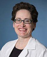 A woman wearing glasses and a white lab coat is smiling for the camera.