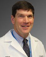 A man in a white coat and tie is smiling for the camera.