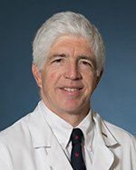 A man in a white coat and tie is smiling for the camera.
