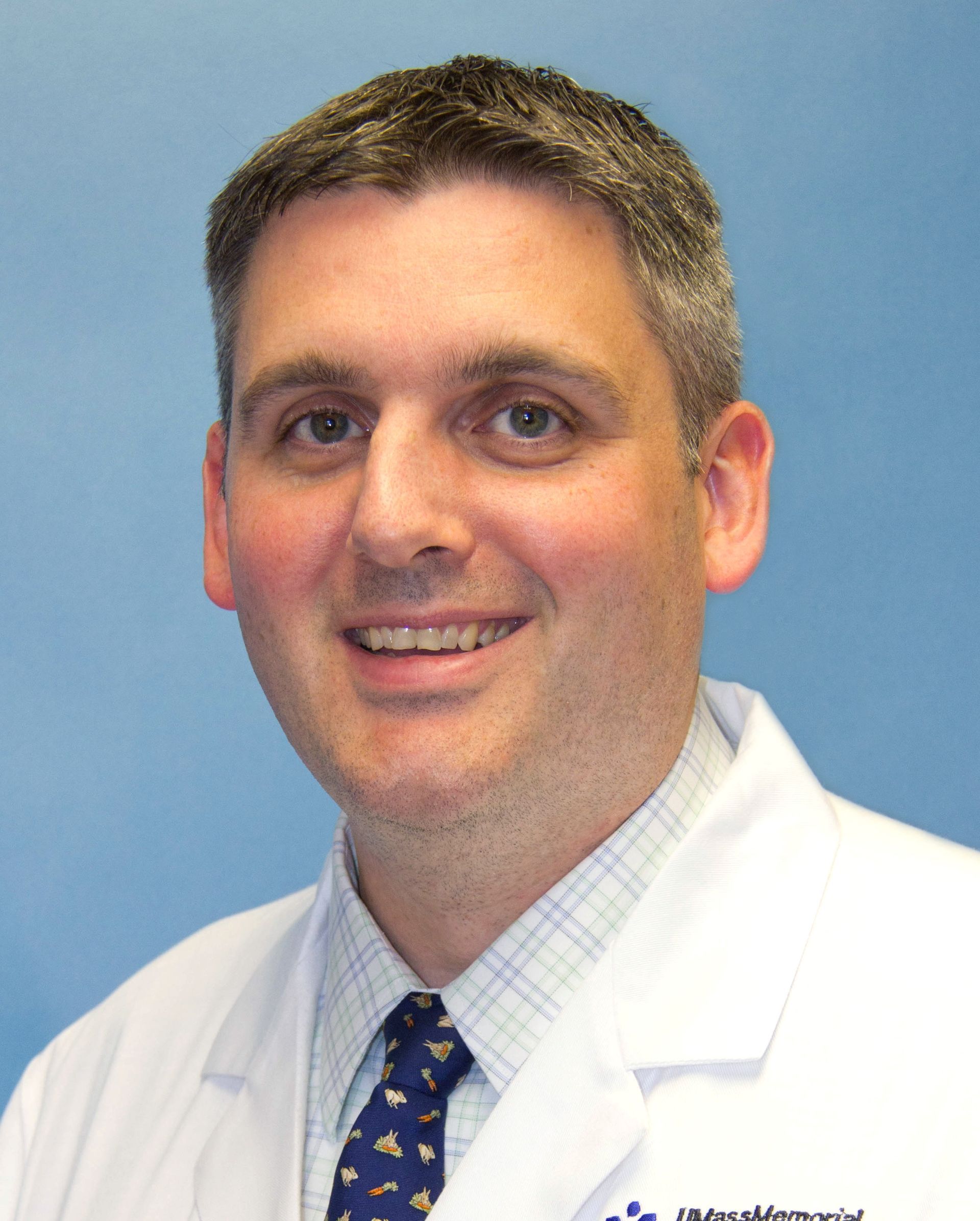 A man in a lab coat and tie is smiling for the camera