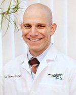 A bald man in a white lab coat and tie is smiling.
