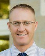 A man wearing glasses and a striped shirt is smiling for the camera.