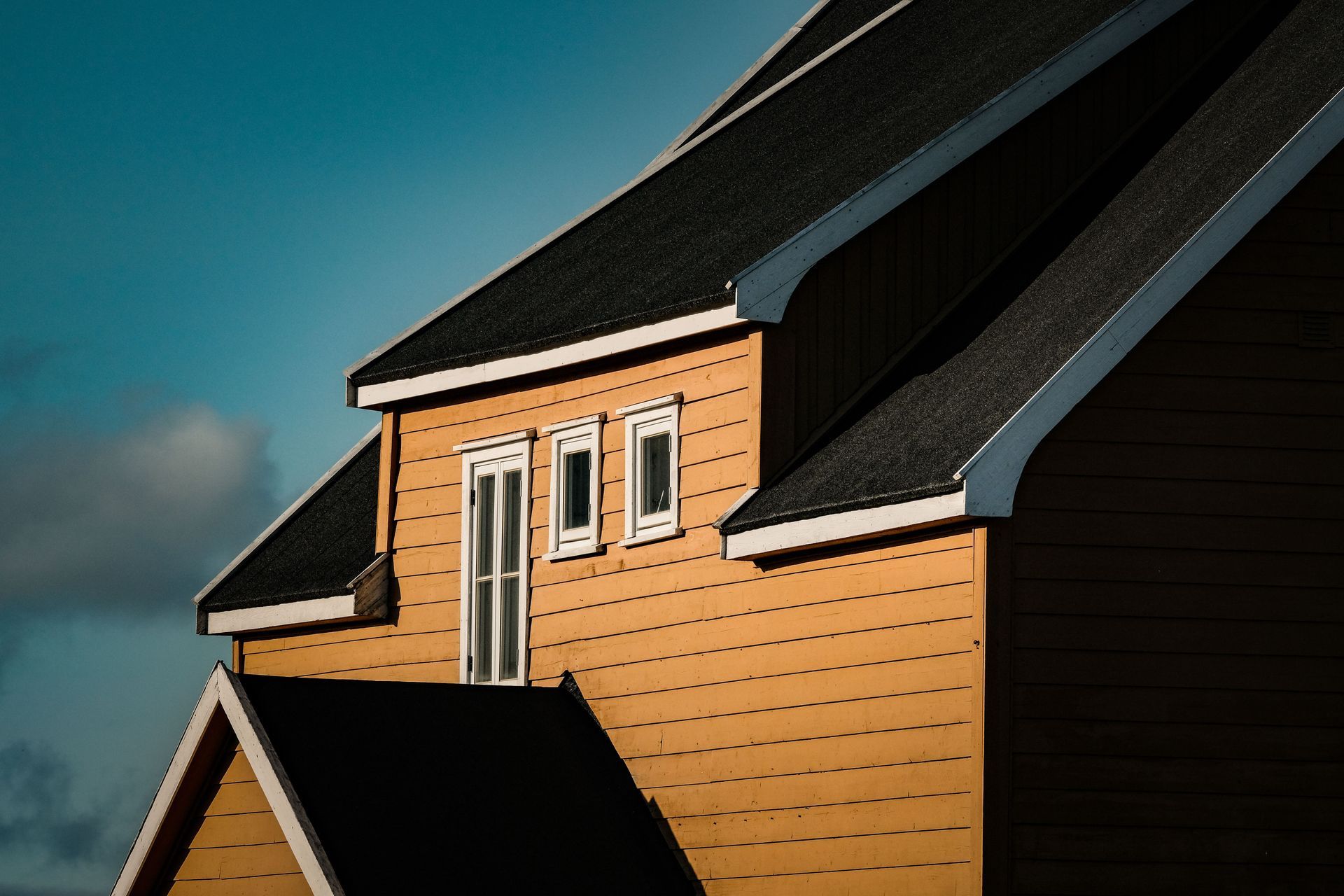 Tan house siding and dark roof against a blue sky, viewed from below
