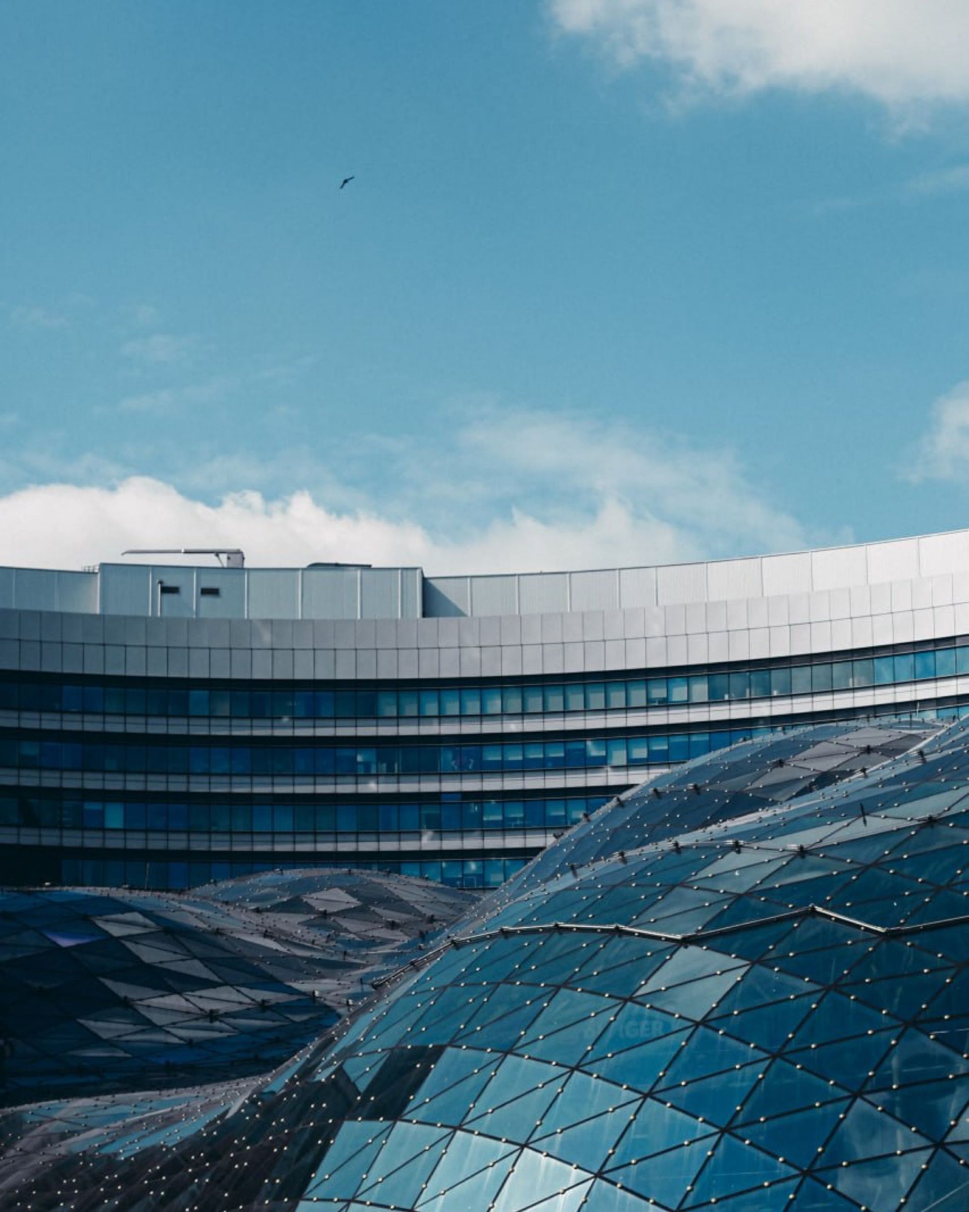 Modern building with curved glass facade under a blue sky, viewed over a textured geometric rooftop