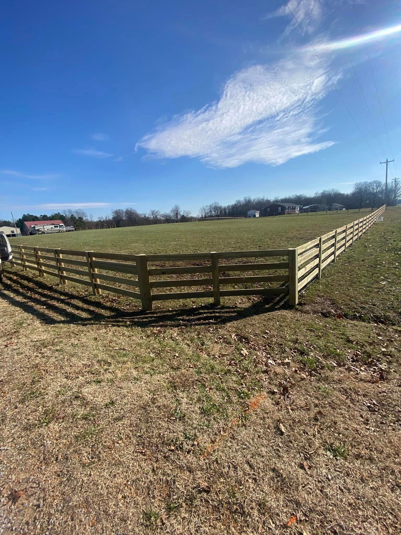 Wooden fence in a field under a blue sky with a few clouds.
