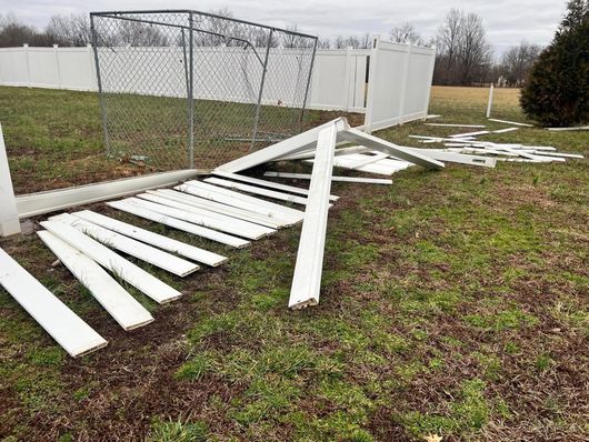 Fallen white picket fence sections on a grassy lawn next to a chain-link fence and a white fence.
